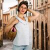 Femme portant une blouse d'été asymétrique sans manches cousue à partir du patron blouse femme Julie de TOSCAminni, debout dans une rue de village pittoresque avec un sac en osier.